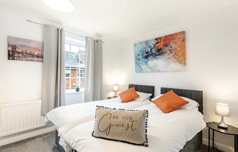 Modern bedroom with double bed, orange cushions, artwork, and window with curtains