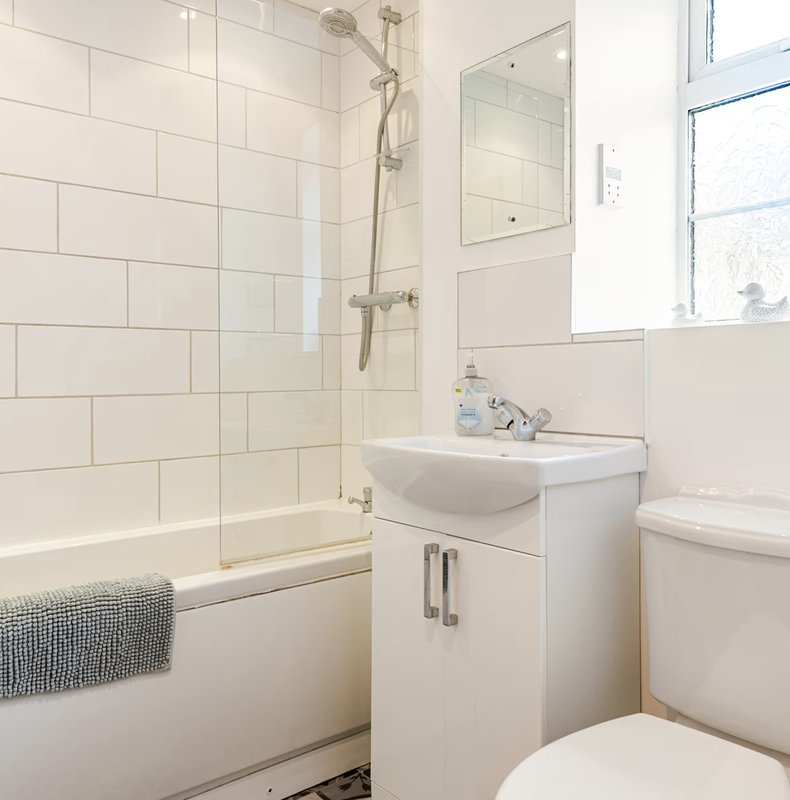 Clean modern bathroom with white subway tile, glass shower enclosure, pedestal sink and toilet