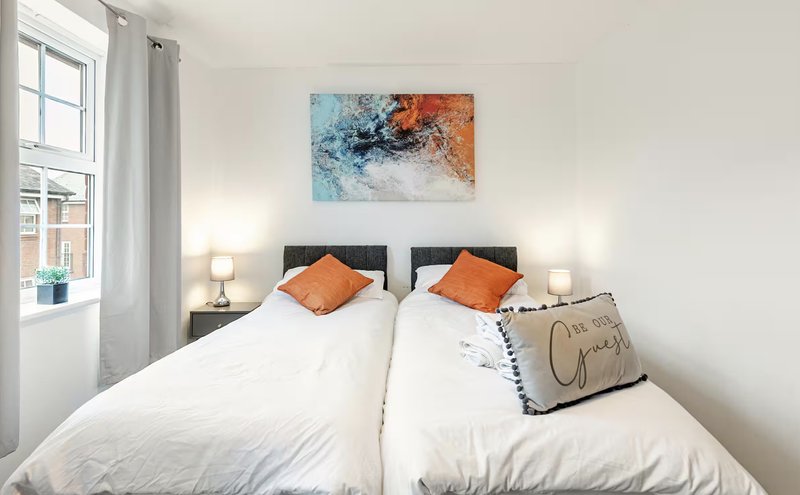 Bright bedroom with two single beds, white bedding, orange cushions and abstract wall art