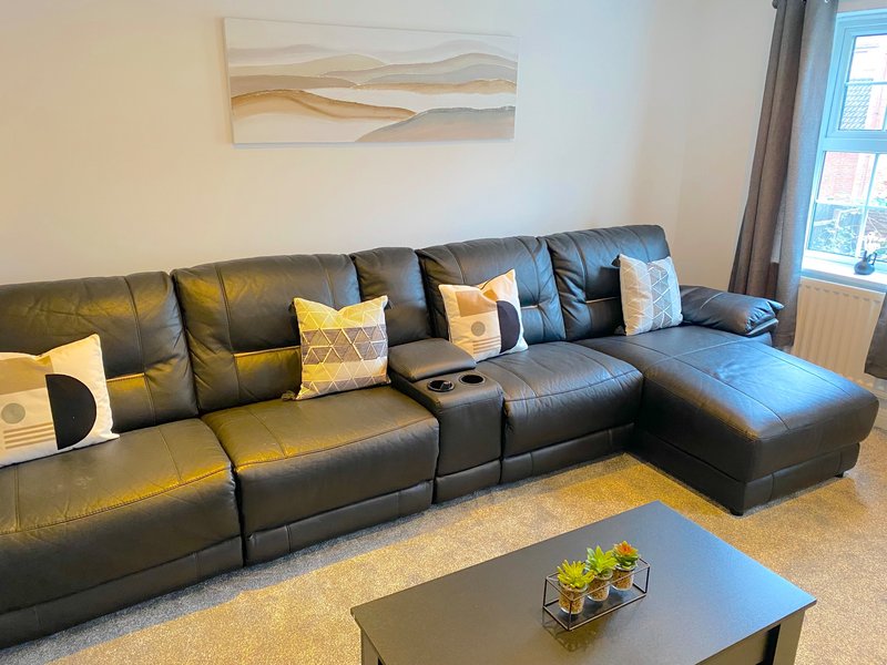Modern living room with black leather sectional sofa, yellow cushions, abstract wall art, and coffee table