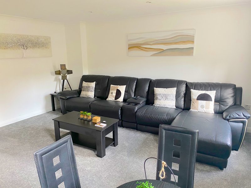 Spacious living room with black leather sectional sofa, dark coffee table, and wall art