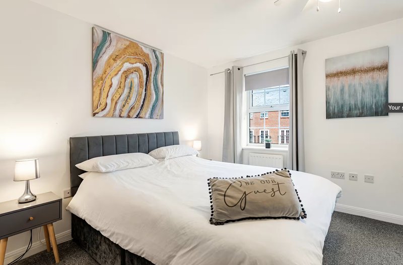 Bright modern bedroom with double bed, grey headboard, bedside lamps, and abstract wall art