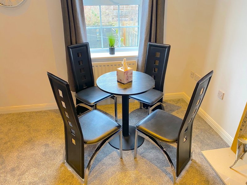 Dining area with small round table, four black chairs, and window view with curtains