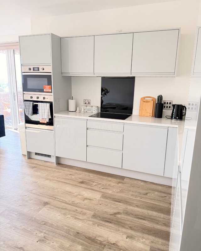 Modern white kitchen with built-in appliances, wooden floor, and countertop accessories