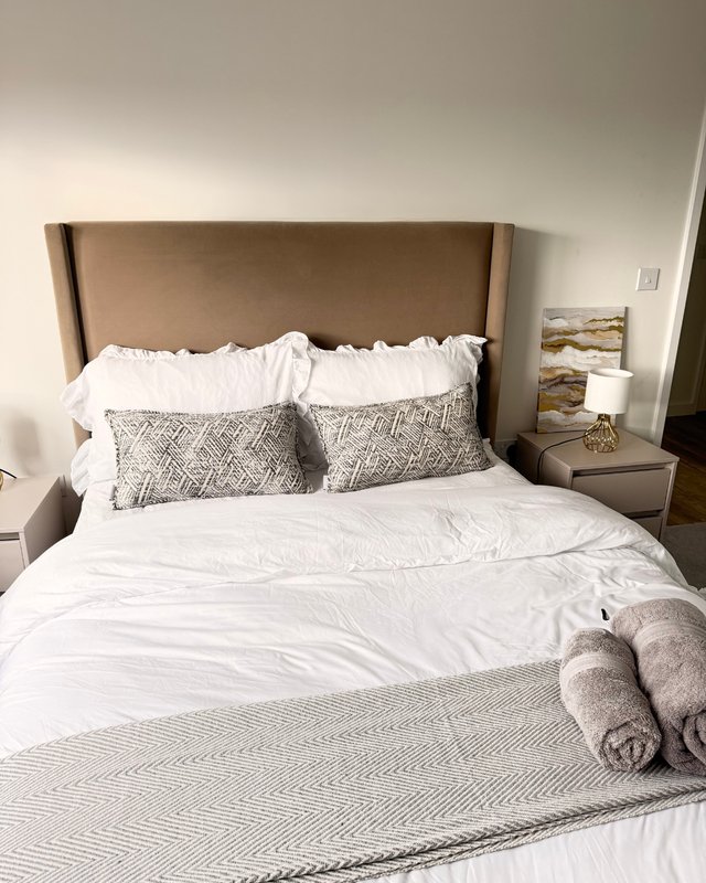 Bedroom with upholstered headboard, white bedding, patterned pillows and rolled towels