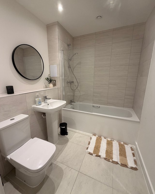 Modern bathroom with toilet, pedestal sink, round mirror, bathtub and shower enclosure