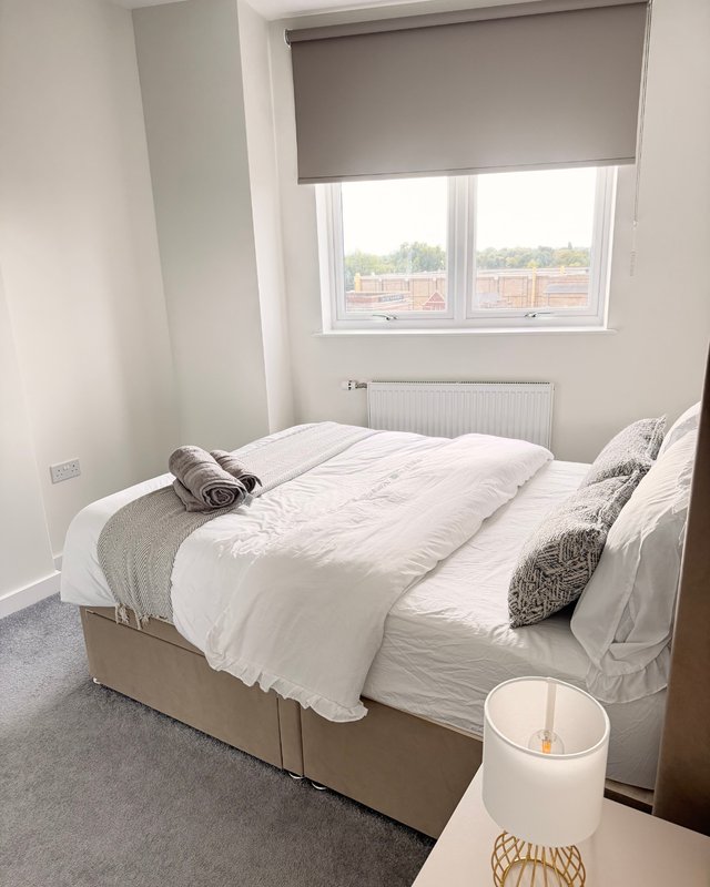 Bright bedroom with double bed, white bedding, grey cushions and window with view