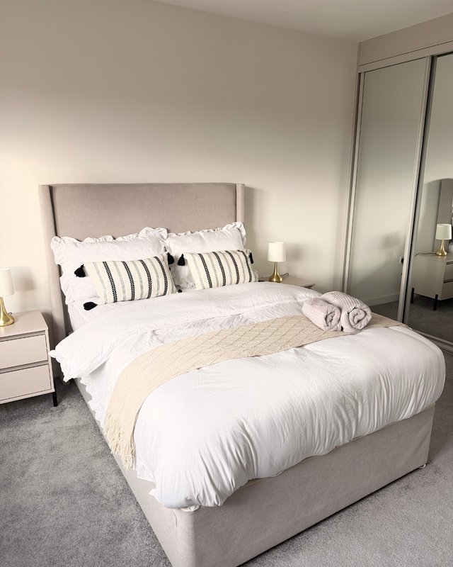 Modern bedroom with grey upholstered bed, striped pillows, white bedding, and mirrored wardrobe