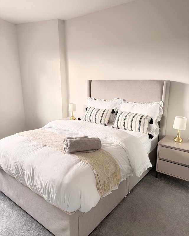Modern bedroom with grey upholstered bed, white bedding, striped pillows and neutral decor