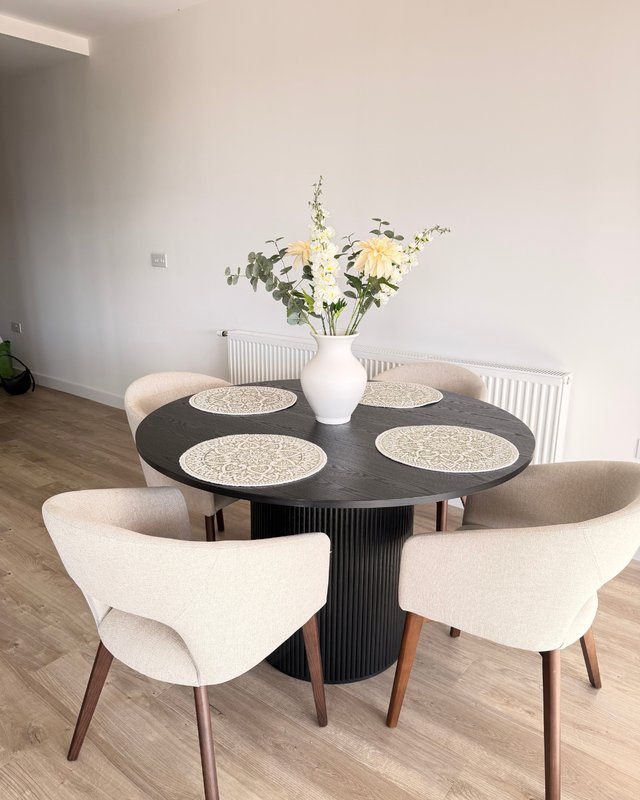 Modern dining room with black round table, four cream chairs, white floral arrangement, and wooden flooring