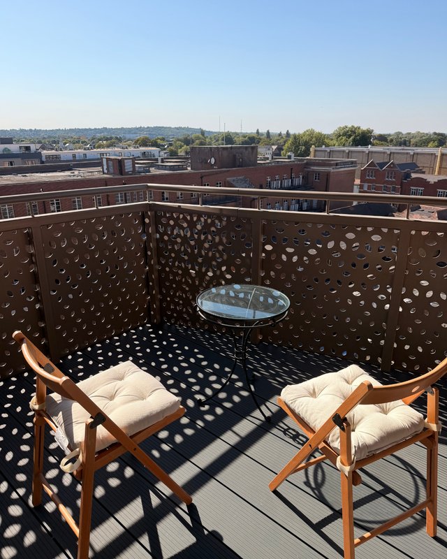 Rooftop terrace with two wooden chairs, cushions, small table, and city skyline view