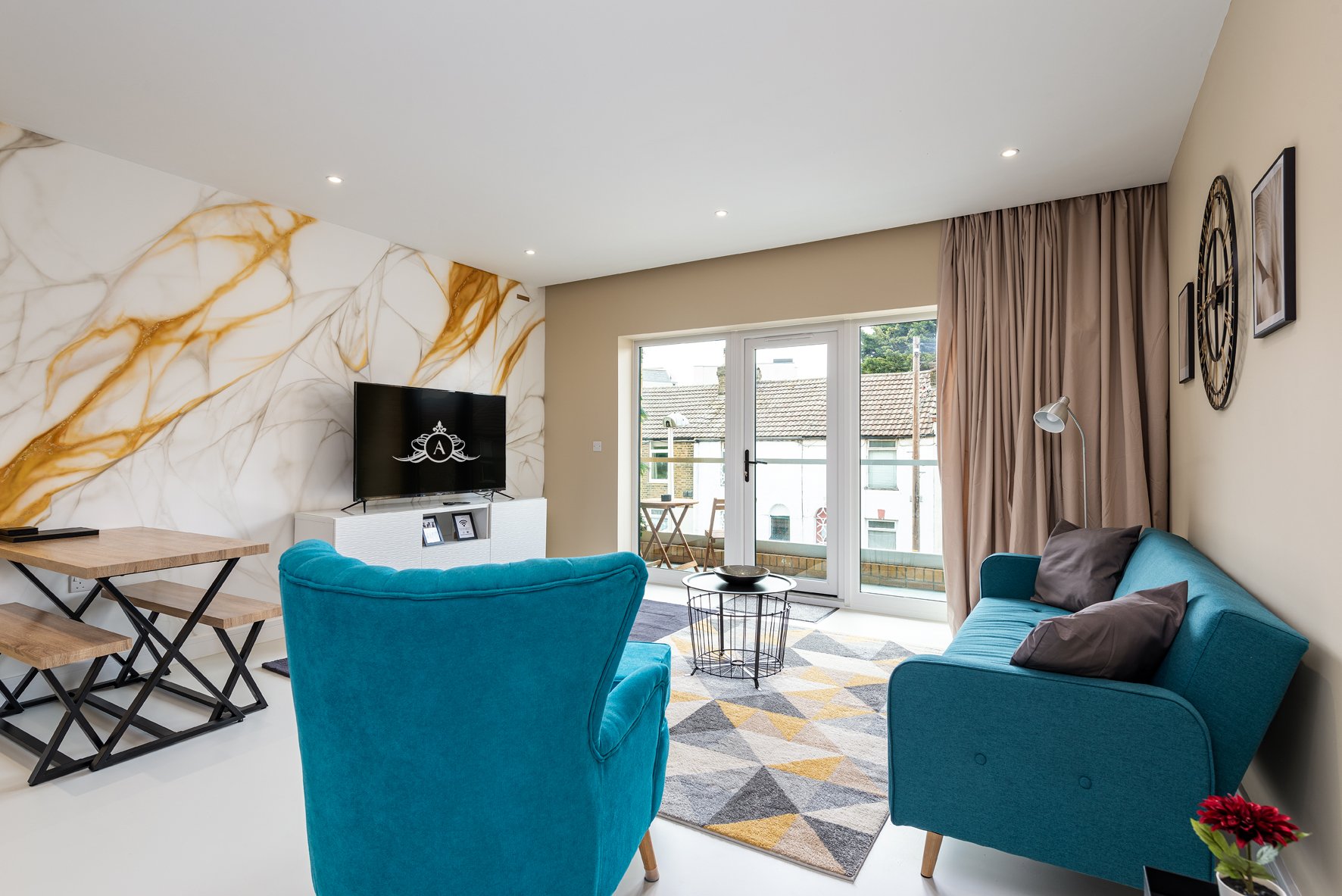 Modern living room with teal armchairs, wall-mounted TV, marble accent wall and patio doors