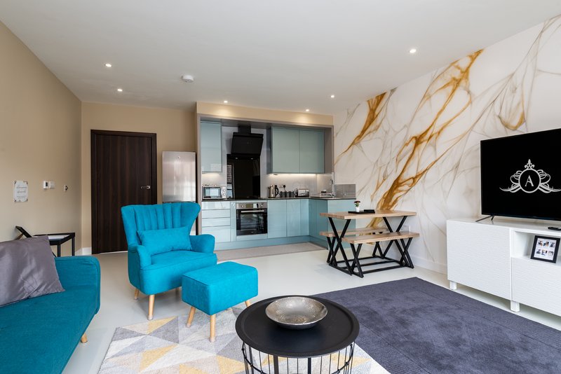 Modern open-plan living space with blue armchair, kitchen, marble backsplash and TV