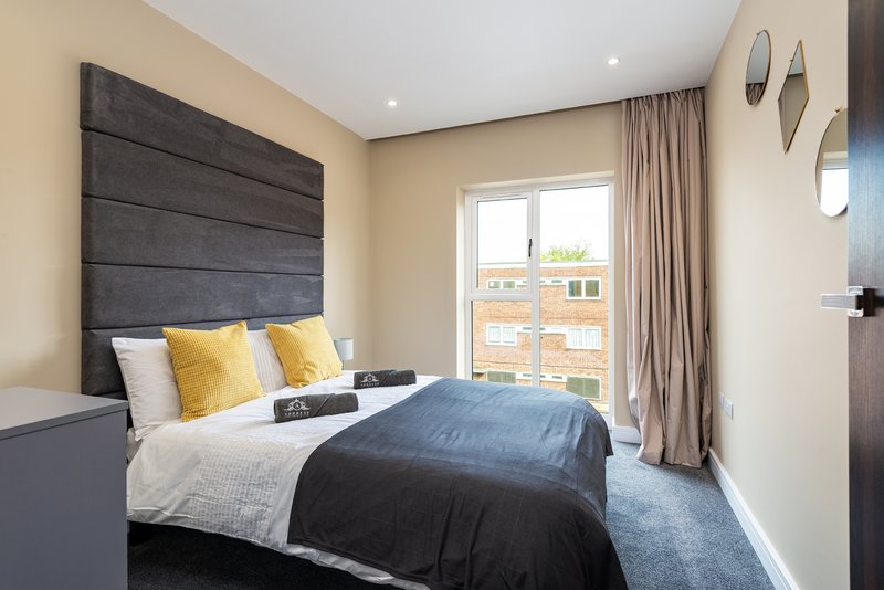 Modern bedroom with dark headboard, double bed, yellow cushions, balcony door and beige walls
