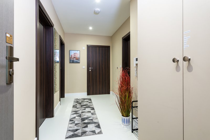 Modern hallway with white tile flooring, dark wooden doors, and decorative red flowers in vase
