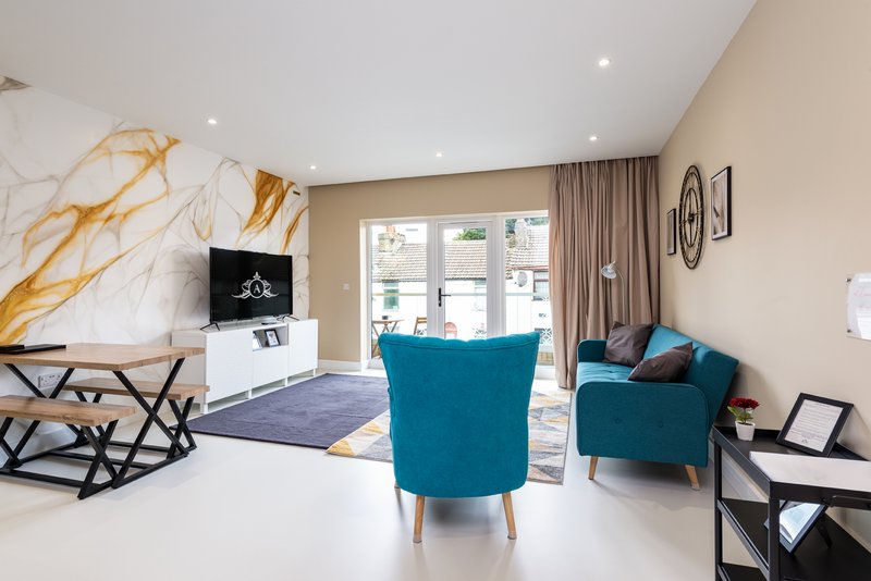 Modern living room with teal armchair, marble accent wall, TV unit, and glass doors to garden