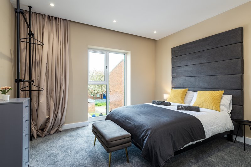 Modern bedroom with double bed, dark headboard, yellow pillows, and patio doors to garden