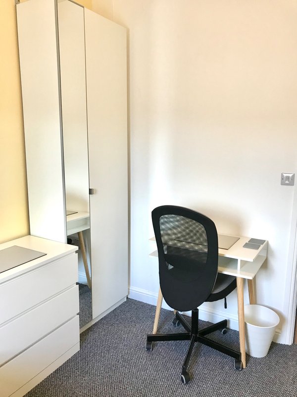 Compact bedroom with mirrored wardrobe, black office chair, small desk and waste bin