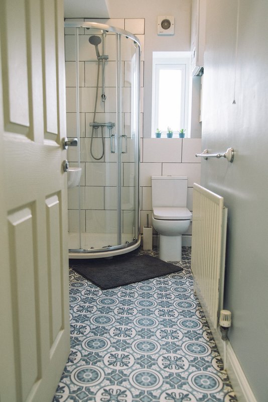Compact bathroom with shower enclosure, toilet, and patterned tile flooring