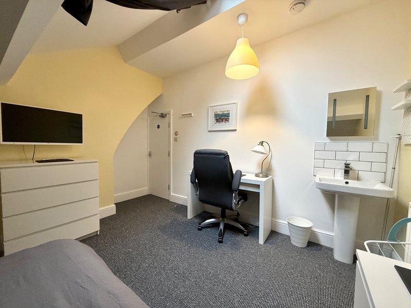 Bedroom with desk, office chair, dresser, wall-mounted TV and en-suite bathroom