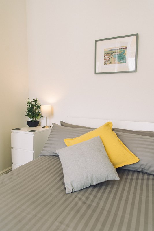 Bedroom with striped bedding, yellow and gray pillows, small table with plant and lamp