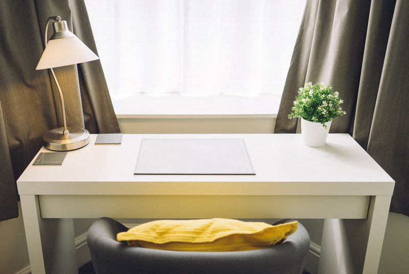 Modern white desk with lamp, potted plant, and window with gray curtains