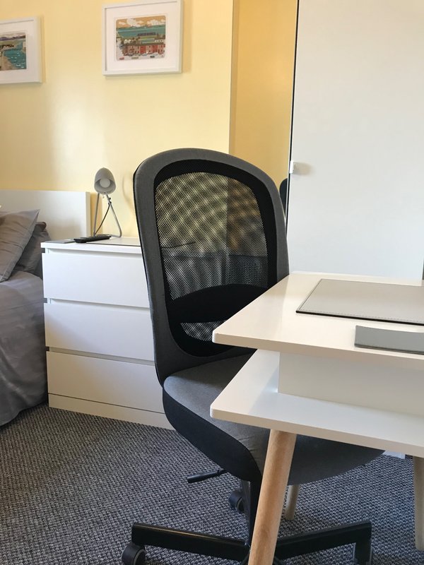 Bedroom workspace with desk, black mesh office chair, white drawers and framed wall art