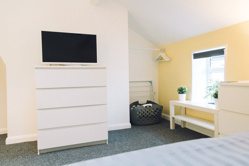 Bright bedroom with white dresser, wall-mounted TV, yellow accent wall, and natural light from window