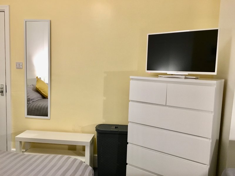 Bedroom with yellow walls, white dresser, flat-screen TV, mirror and bench seating