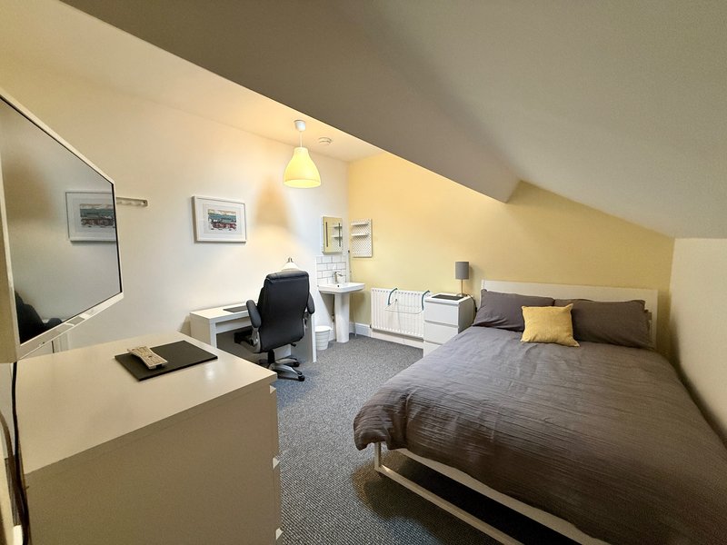 Attic bedroom with double bed, desk, chair, mirror and yellow accent wall