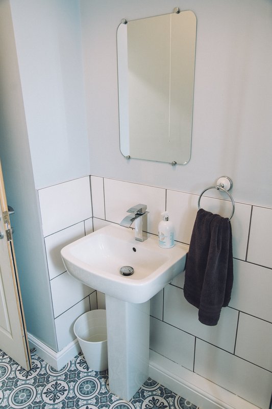 Bathroom with pedestal sink, wall-mounted mirror, subway tile, and black towel rack
