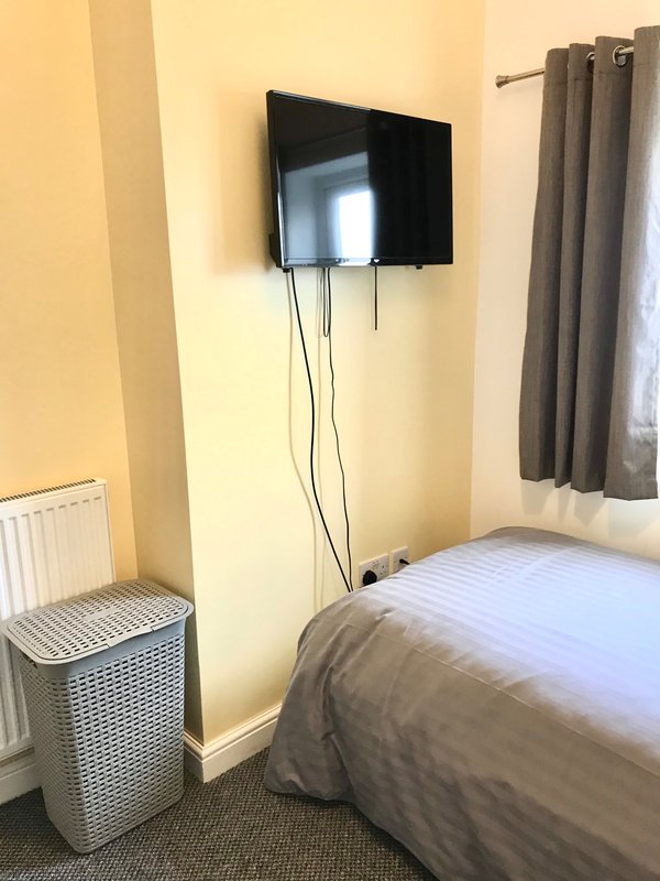 Bedroom with single bed, wall-mounted TV, laundry basket and grey curtains