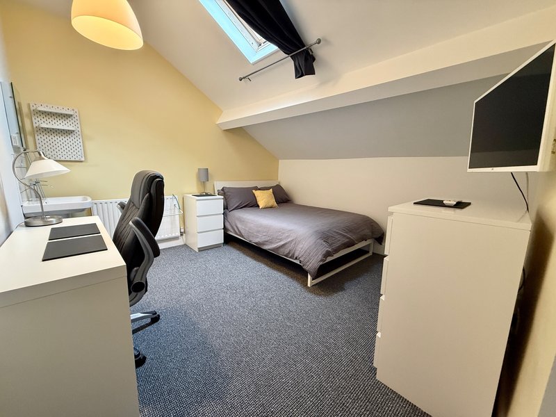 Bedroom with single bed, desk, office chair, TV and white storage cabinet