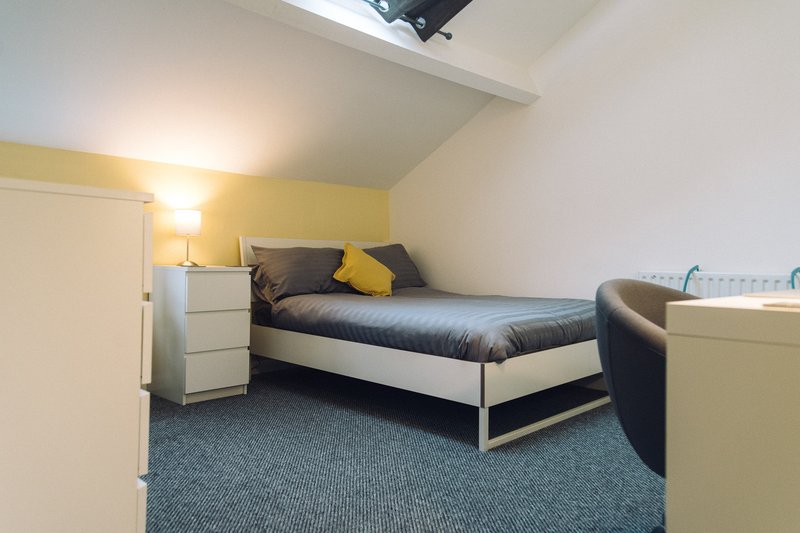 Attic bedroom with single bed, yellow accent wall, bedside lamp and storage dresser