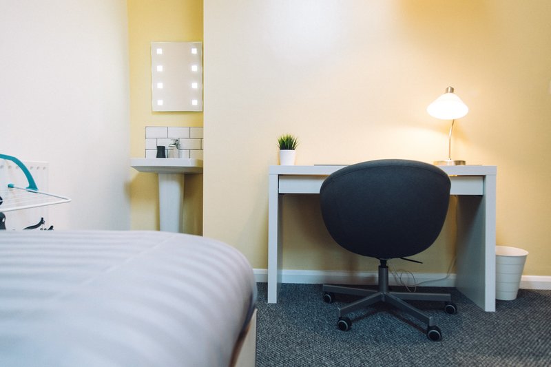 Bedroom with single bed, desk with black chair, mirror, lamp and potted plant