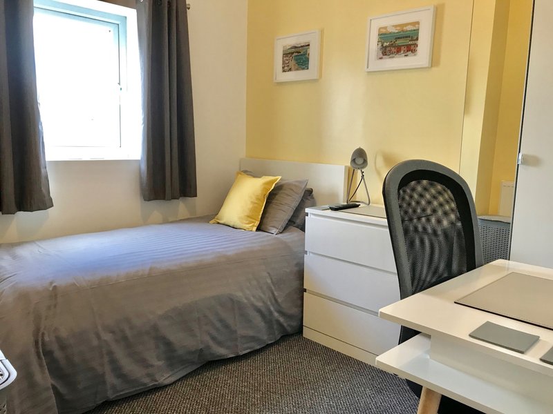Bedroom with single bed, desk, chair, window with curtains and yellow walls