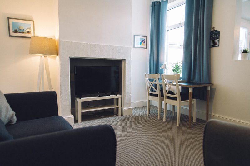 Spacious living room with dark sofas, TV stand, dining table and chairs by window