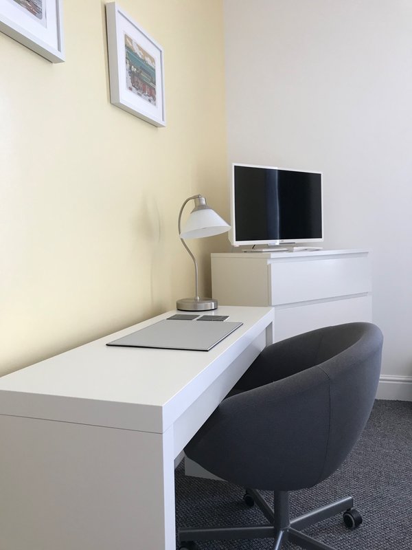 Modern workspace with white desk, black chair, monitor, lamp, and framed wall art
