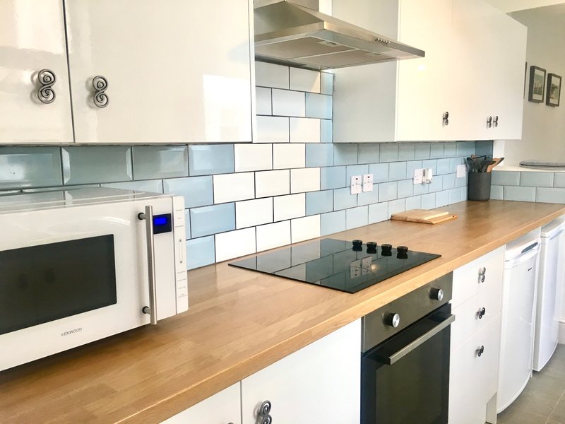 Modern kitchen with white cabinets, wooden countertop, blue tile backsplash and integrated appliances