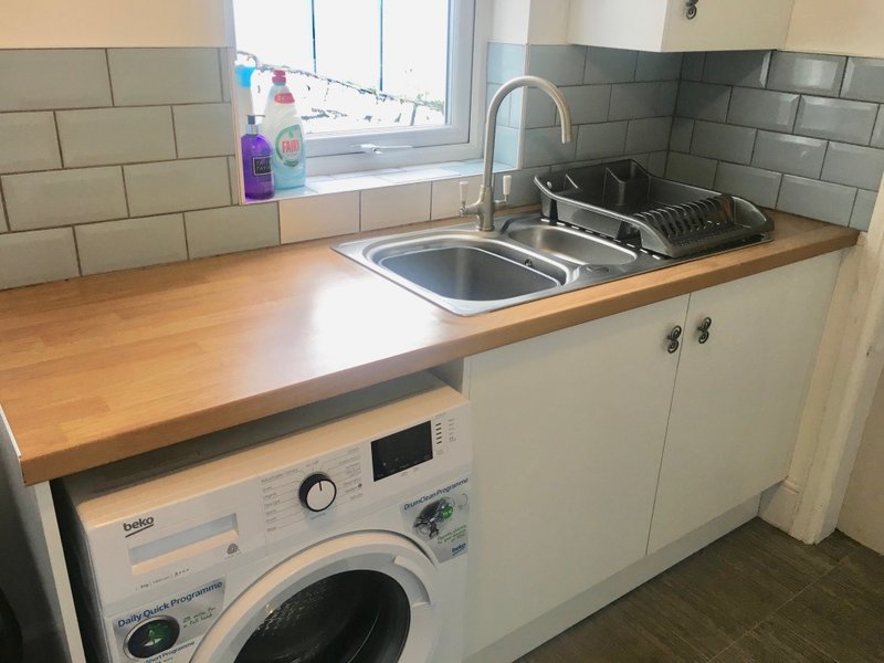 Kitchen with sink, washing machine, wooden countertop and subway tile backsplash
