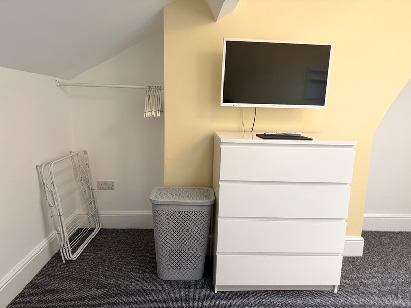 Modern bedroom with white dresser, wall-mounted TV, laundry basket and folding chair