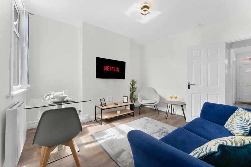 Modern living room with blue sofa, desk, TV mounted on wall, and wooden flooring
