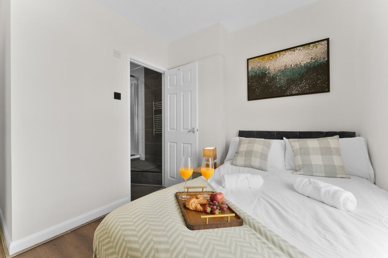 Bright bedroom with double bed, white bedding, framed landscape art, and wooden floor