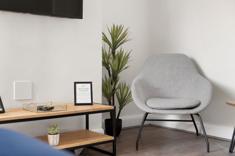 Modern living room with gray upholstered chair, wooden desk, potted plant and minimalist decor