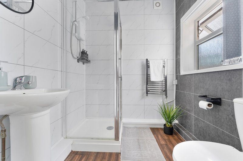 Modern bathroom with white tiles, glass shower enclosure, pedestal sink and toilet