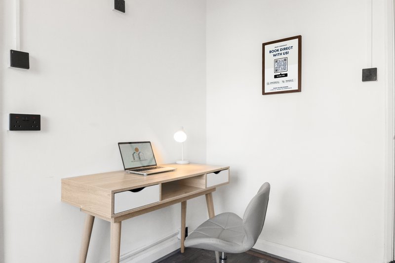 Minimalist home office with wooden desk, gray chair, laptop and wall-mounted artwork