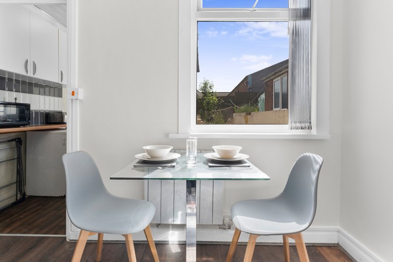 Modern dining area with small white table, two gray chairs, and kitchen view through window