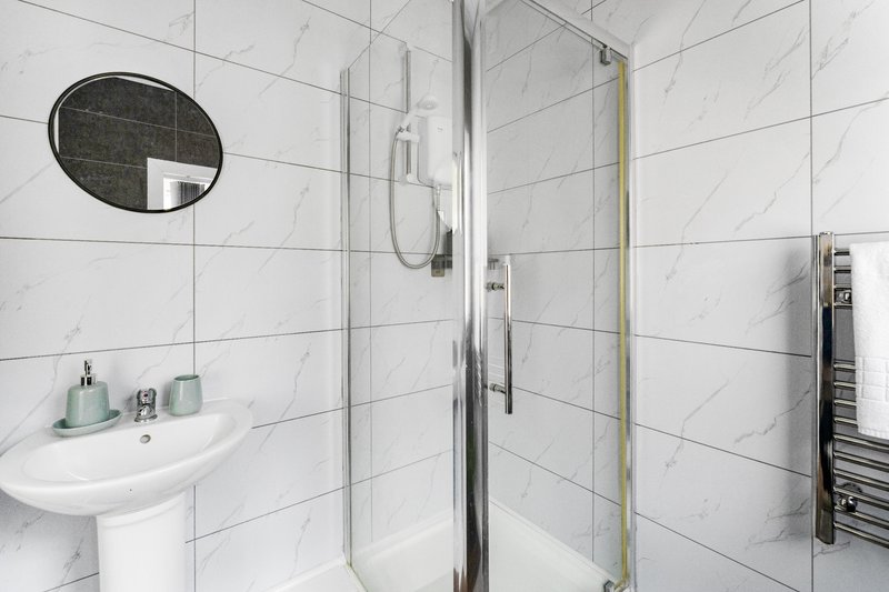Modern white marble bathroom with walk-in shower, pedestal sink and round mirror