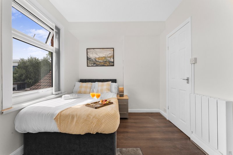 Bright bedroom with double bed, large window, wooden floor and framed landscape artwork