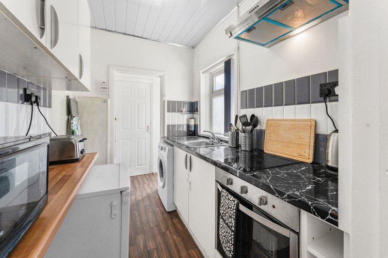 Galley kitchen with white cabinetry, black marble countertops, stainless steel appliances and wood flooring